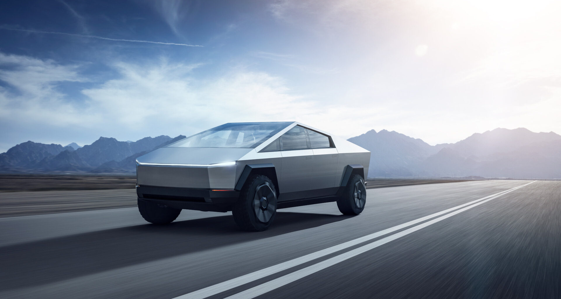 A Tesla Cybertruck on an empty road with mountains in the distance.