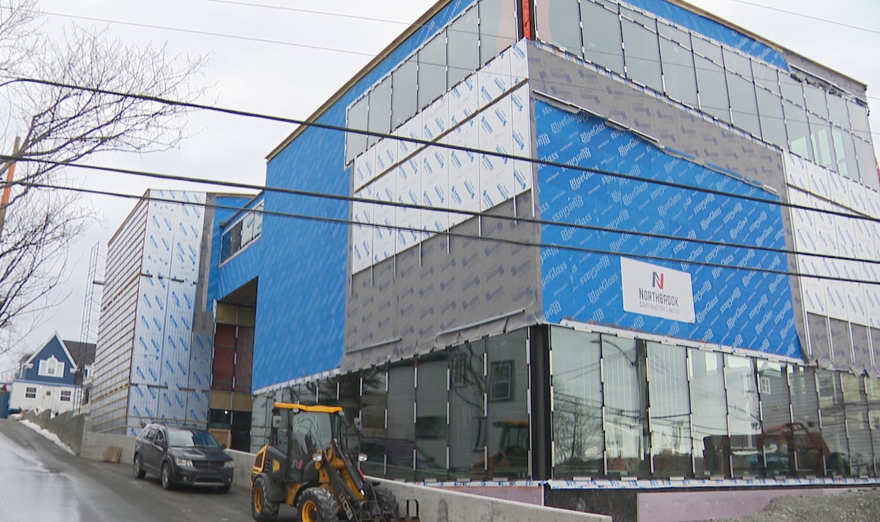 Heavy equipment is parked outside a large glass and metal building under construction on a grey, winter day.