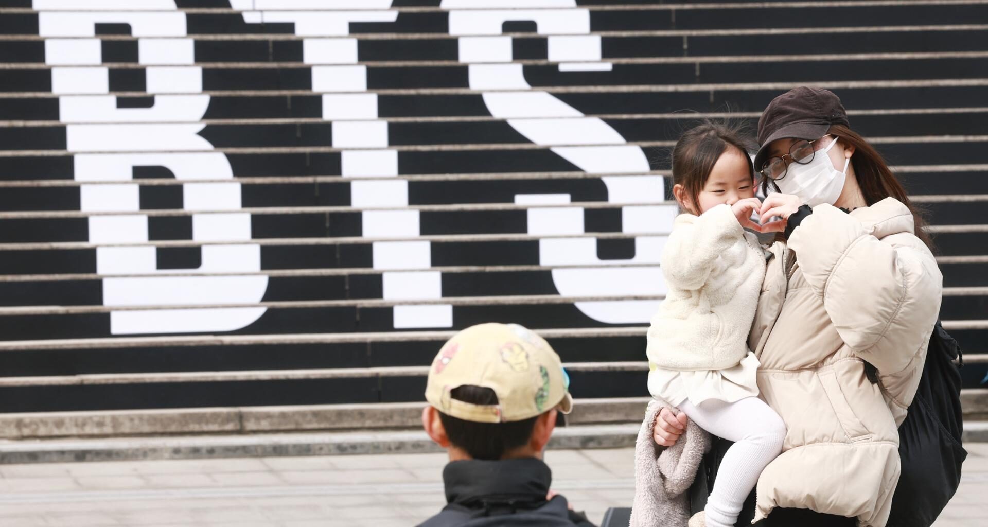 A family of foreign tourists poses in front of a promotional ad for a concert by K-pop boy band BTS, on the steps of the Sejong Center for the Performing Arts in Jongno District, Seoul, March 11. Yonhap