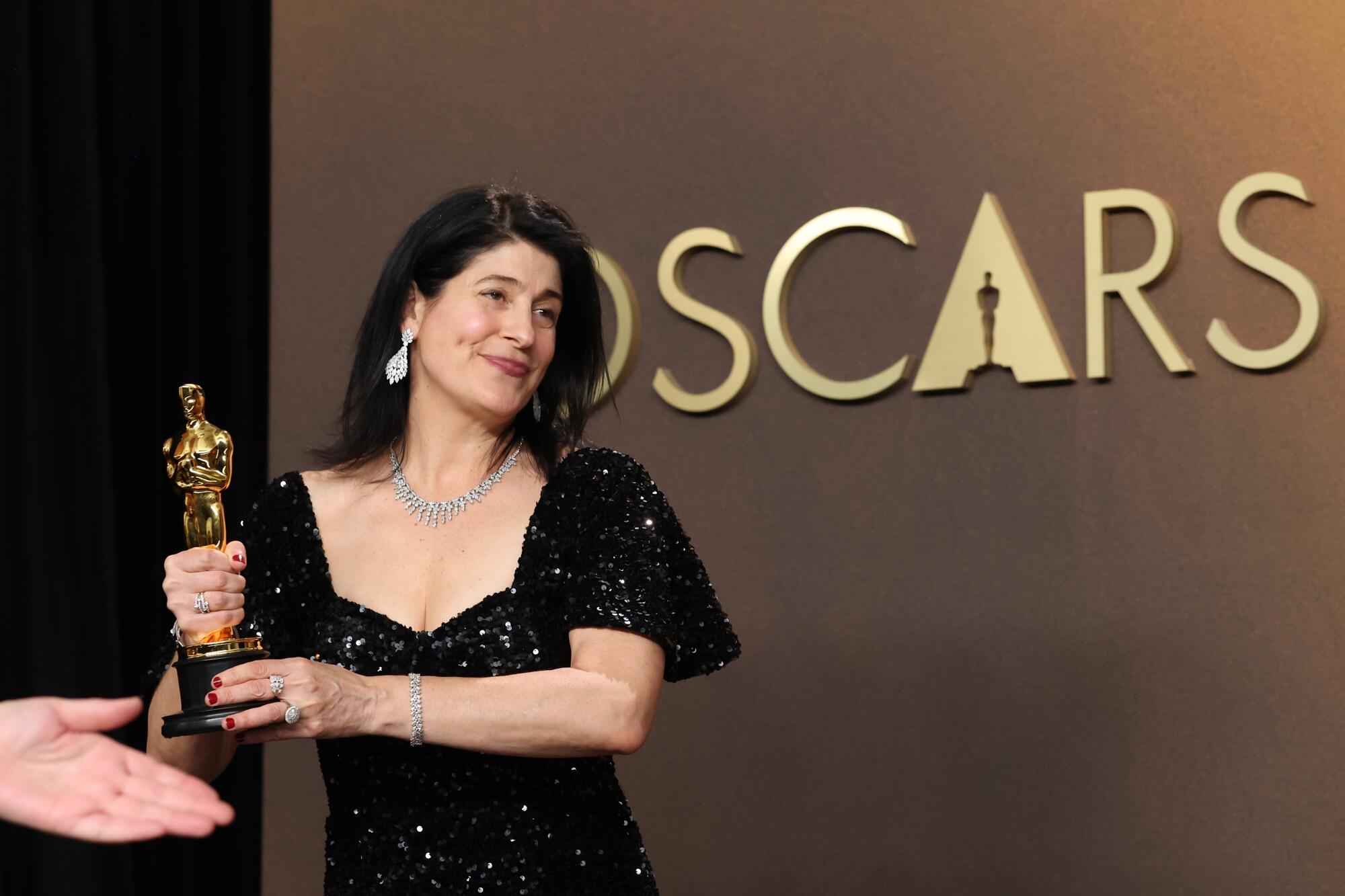 A woman in a black shimmering dress holding a golden Oscar statuette with both hands.