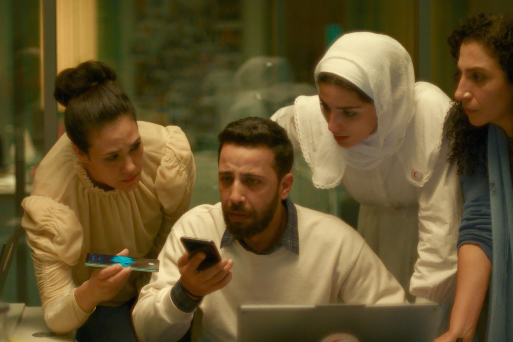 Three woman bend over a man looking at a cellphone in a scene from a movie