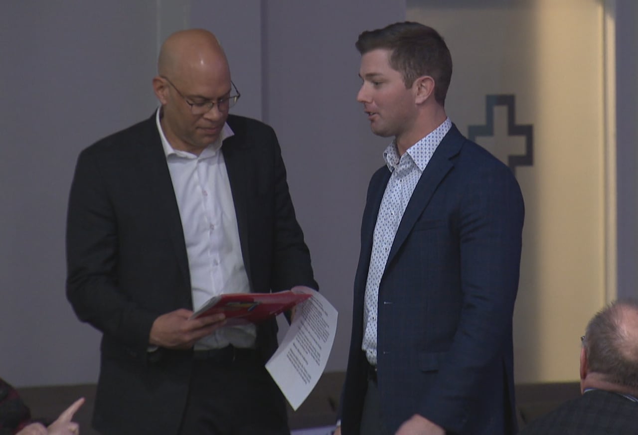 Two men talk at the front of the room. 