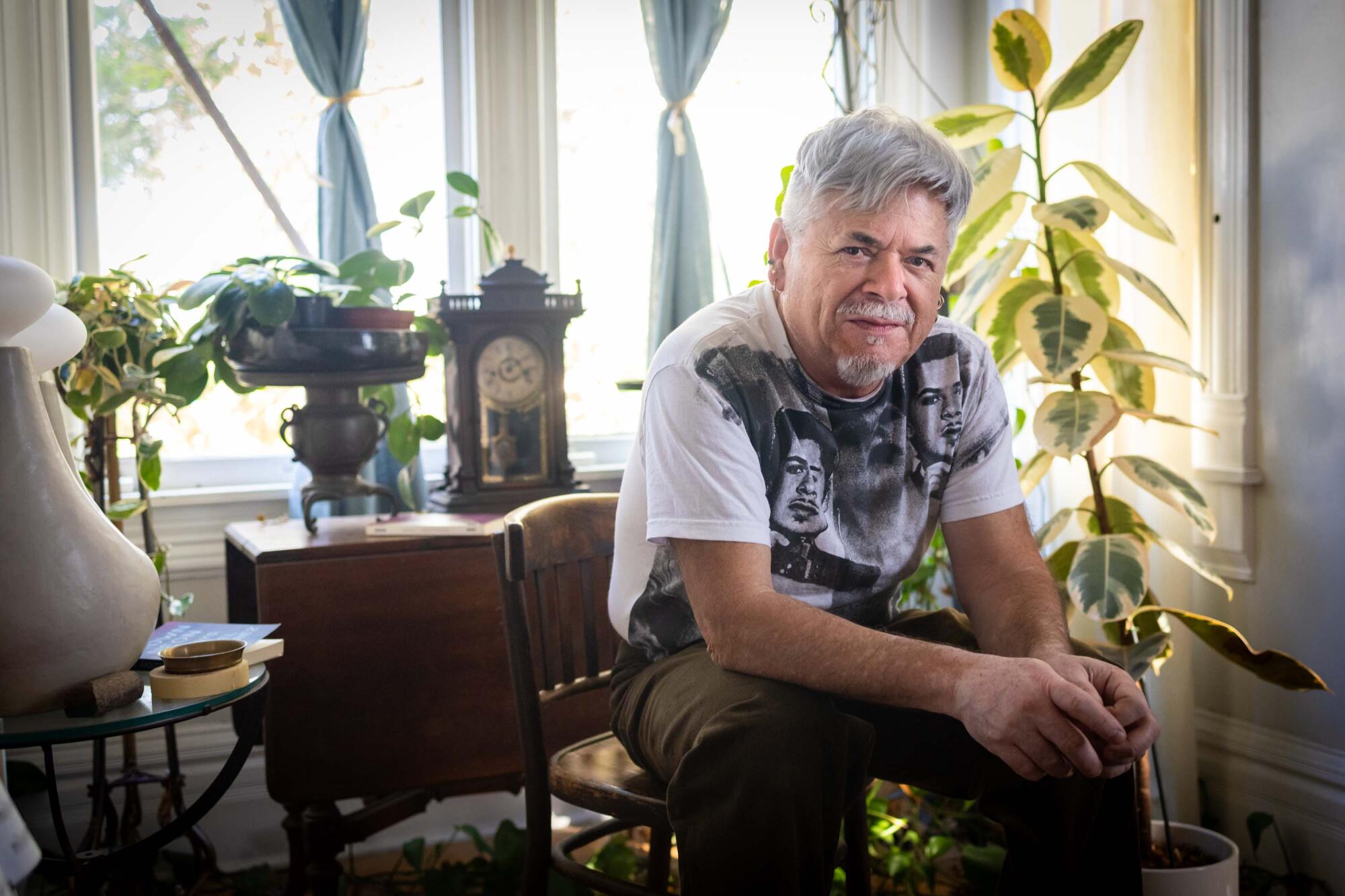 A man seated on a wooden chair, surrounded by furniture and plants