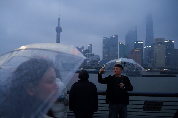 People take selfie photos along the Shanghai Bund as the skyline of Pudong is seen across the Huangpu River during rainy weather in Shanghai, Monday, March 16, 2026. (AP Photo/Vincent Thian)