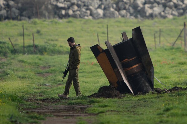 An Israeli soldier stands next to a fragment of a missile fired from Iran and intercepted by Israeli air defense system embedded in an open field in the Israeli-controlled Golan Heights, March 19, 2026. (AP Photo/Ohad Zwigenberg, File)