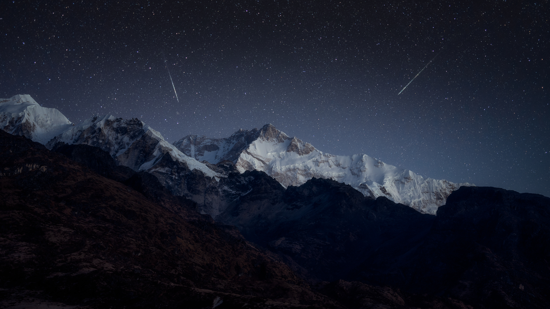 Shooting stars are pictured streaking downward through the night sky above a snowy mountain range.