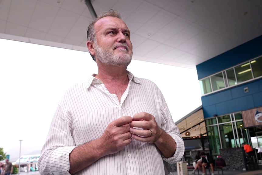 A man wearing a buttoned white shirt plays with his fingers with a worried expression on his face.