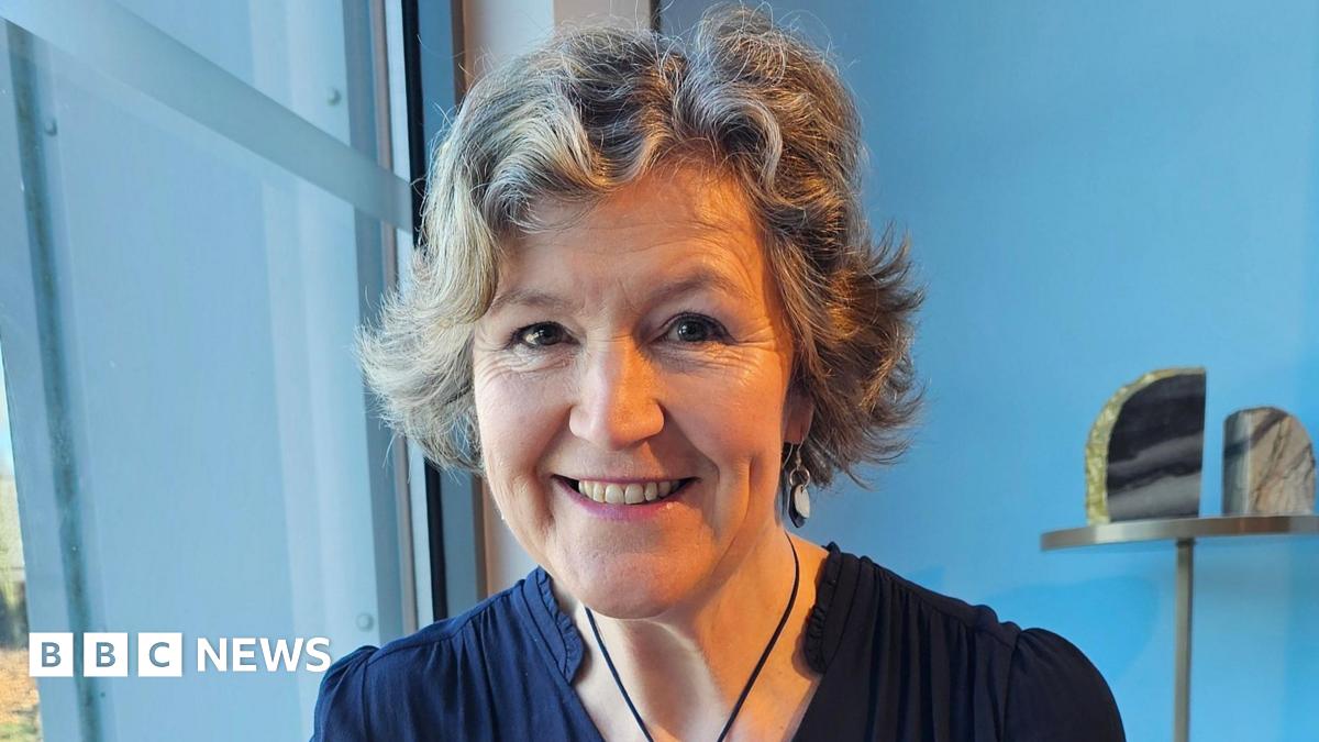 A woman in a navy blue dress smiling at the camera while sitting in front of a blue wall.