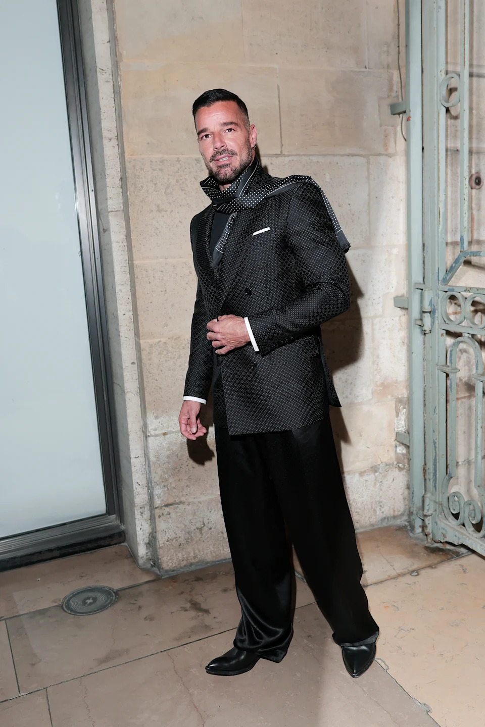 Person in a stylish polka dot suit with a high collar and shiny shoes, posing confidently outside at an event