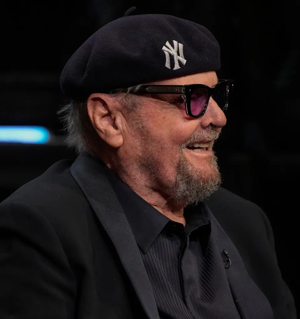 Jack Nicholson in sunglasses and beret, wearing a dark blazer, smiling while seated at an event