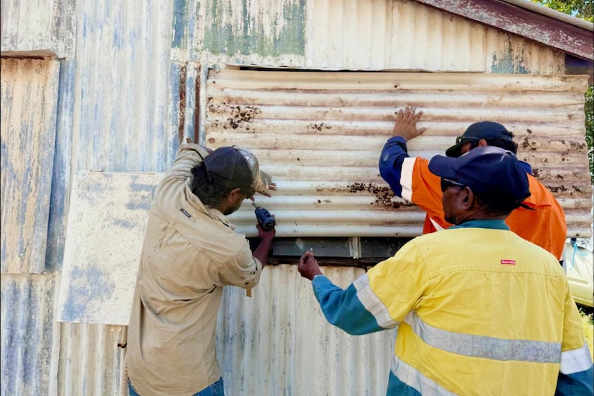 three men drilling a corrugated iron slab onto an old building