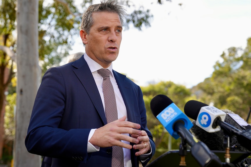 Man in suit speaks outside with microphones