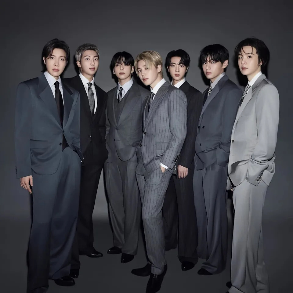BTS—Jin, Suga, J-Hope, RM, Jimin, V, and Jung Kook—in stylish suits pose together against a dark background. This is a photo from their new album ARIRANG