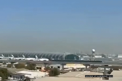 A video still of an airport with planes parked at a terminal building under a hazy sky.