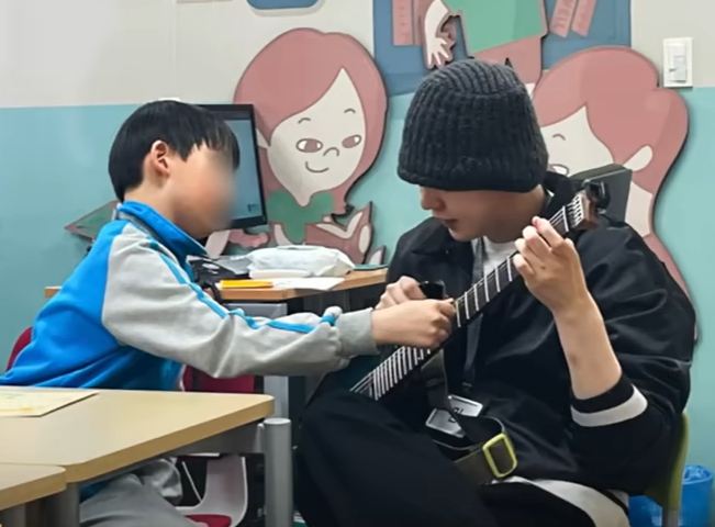 Suga of boy band BTS plays a guitar with a child patient at Severance Hospital in Seodaemun District, western Seoul, during a visit to the hospital on June 26, 2025. [SCREEN CAPTURE]