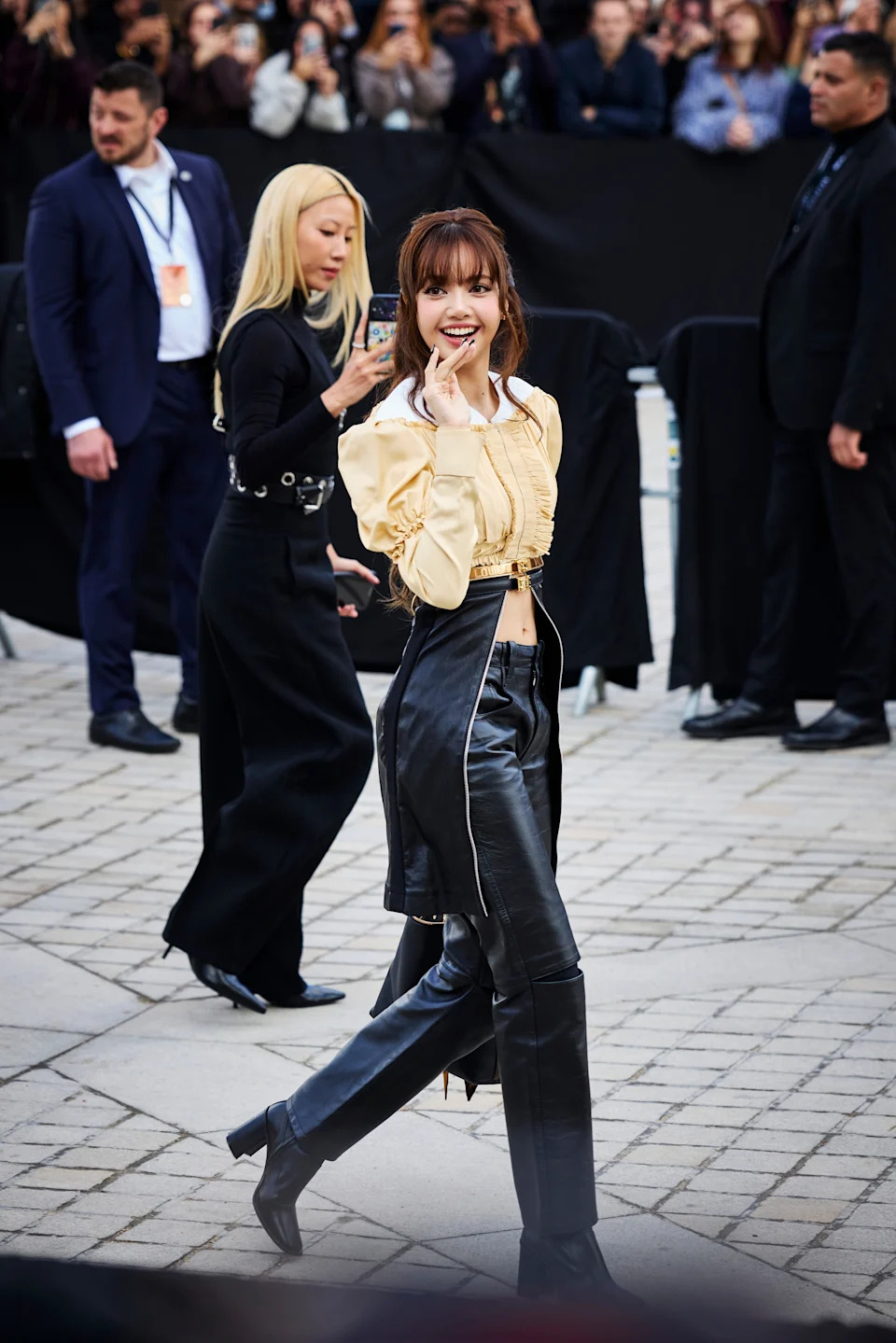 Celebrity in leather pants and a stylish top poses smiling while walking at an event