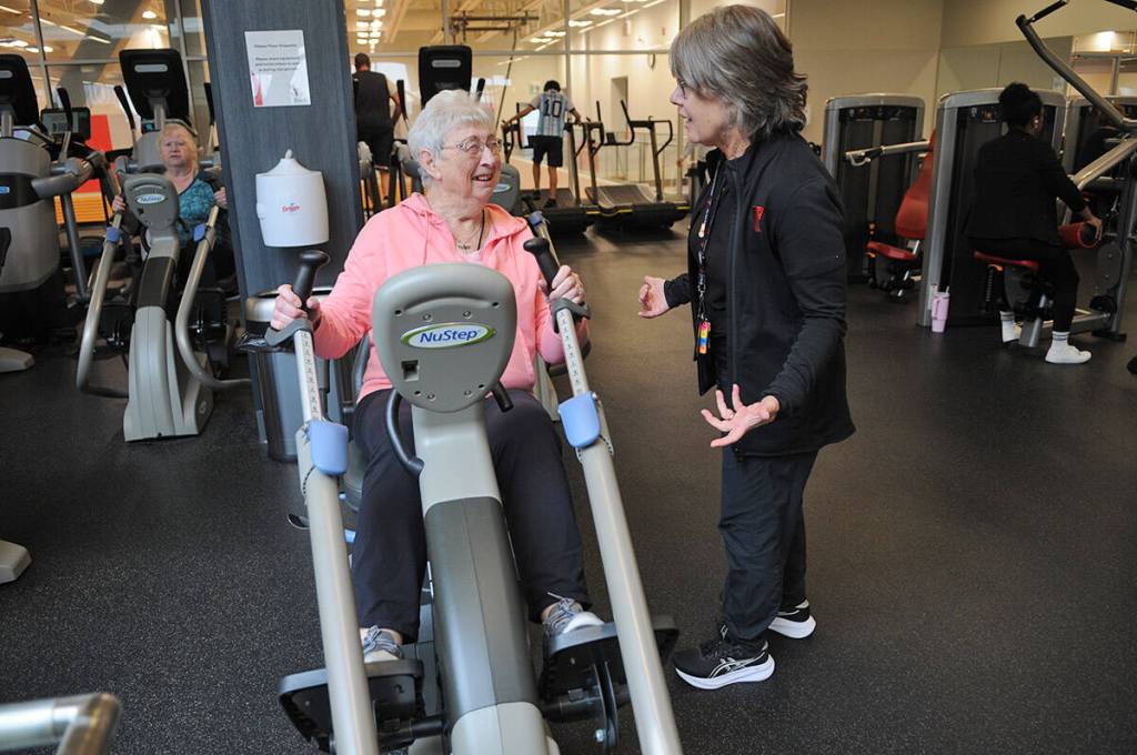Gillian Phillips, 86, uses a NuStep machine while sharing a laugh with Karen Price, general manager of the Bob Chan-Kent Family YMCA, in Chilliwack on March 19, 2026. (Jenna Hauck/ Chilliwack Progress)