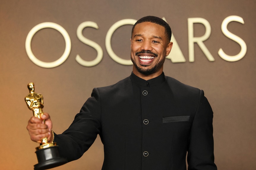 Michael B Jordan in Oscars photo room with Oscars written behind him, holding a trophy