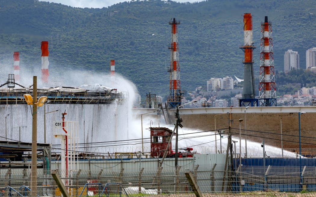 Firefighters attempt to extinguish a fire following a projectile impact on a refinery in Israel's northern city of Haifa on March 30, 2026. Israel and Iran exchanged more missile fire on March 30 as concerns that the US might escalate the Middle East conflict by launching ground raids against the Islamic republic's Gulf islands sent oil prices soaring.