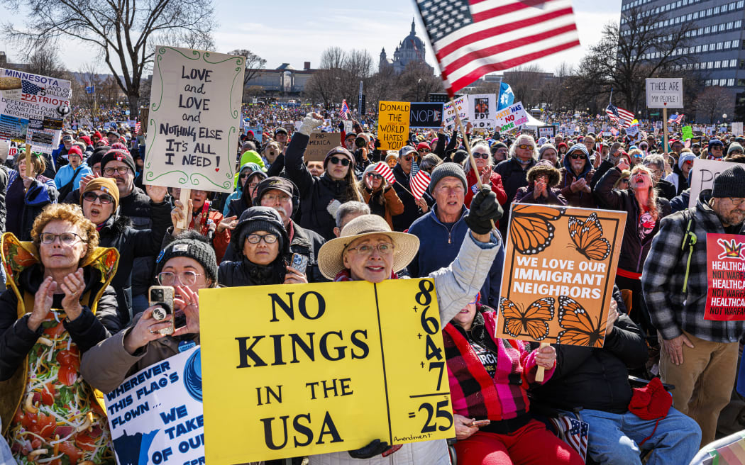 A woman holds a sign and waves a US flag as a large crowd gathers outside the Minnesota State Capitol during the 