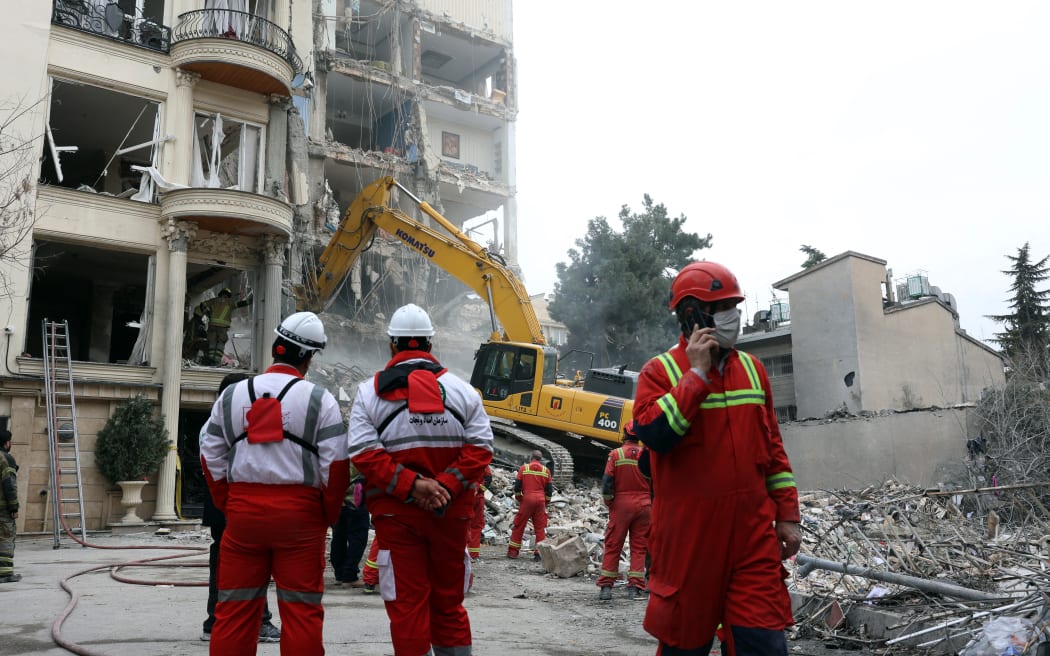 Iranian firefighters with the help of an excavator clear rubble from a destroyed residential building in northern Tehran on March 23, 2026. A series of strong explosions were heard in the Iranian capital on March 23, an AFP journalist said, as the war with the United States and Israel raged for its fourth week. On February 28, Israel and the United States launched strikes on Iran killing its supreme leader and triggering a war that spread across the Middle East and unleashed chaos across global markets and sent oil prices soaring. (Photo by AFP) /