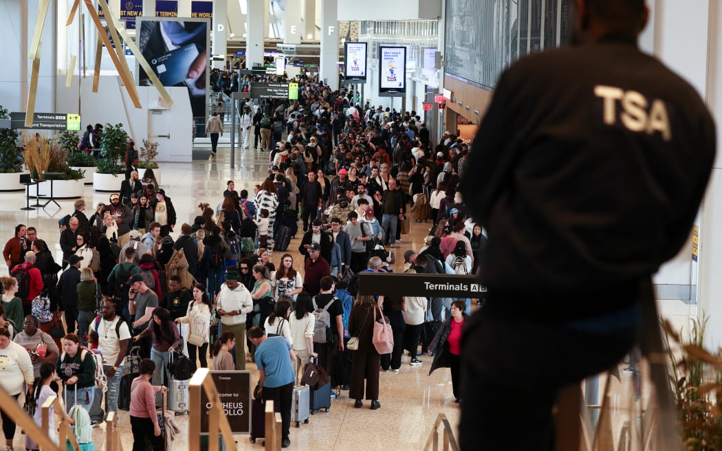 A Transportation Security Administration (TSA) agent looks on passengers queue to go through security at New York's LaGuardia airport on March 22, 2026. Immigration agents will be deployed in US airports beginning March 23, aiming to alleviate soaring congestion at security screenings amid a weeks-long budget standoff over President Donald Trump's mass deportation drive, officials said. Trump announced the extraordinary move in a social media post Sunday morning, sending officials racing to quickly develop a plan. (Photo by CHARLY TRIBALLEAU / AFP)