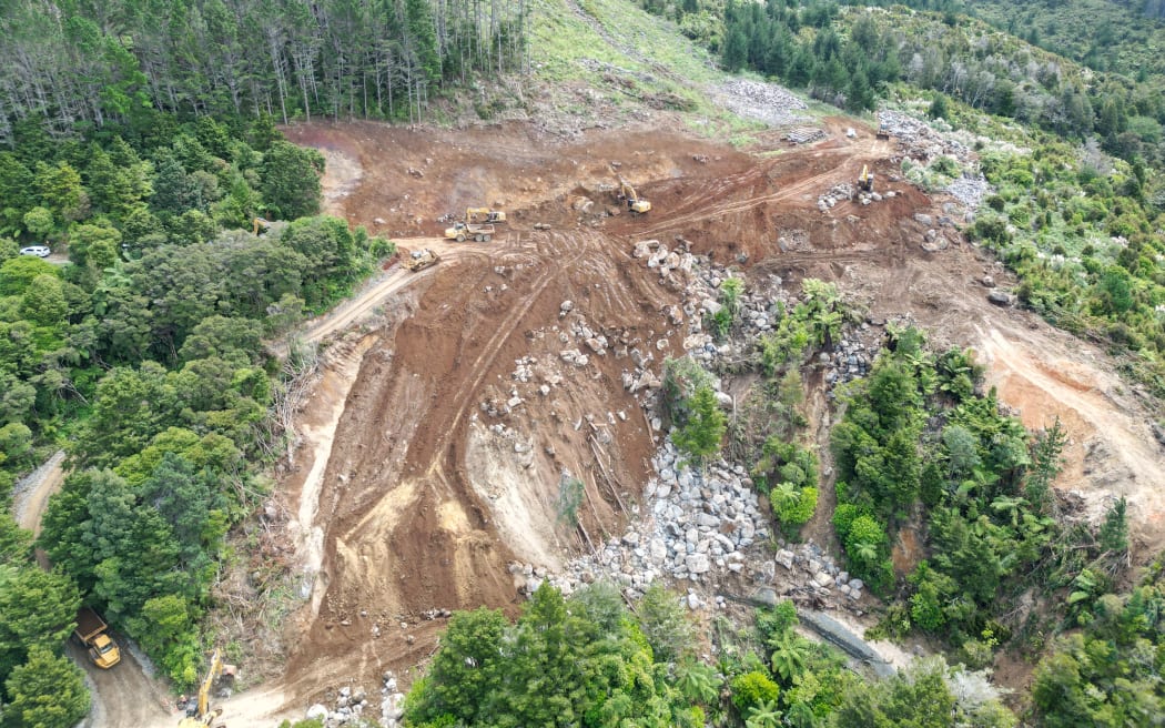 A worker standing beside the digger at the bottom left-hand corner of this aerial photo appears no bigger than a tiny orange freckle. It illustrates the massive scale of Helena Bay hill landslide clearance. Hundreds of bigger-than-truck-sized boulders uncovered en route are adding extra challenges.