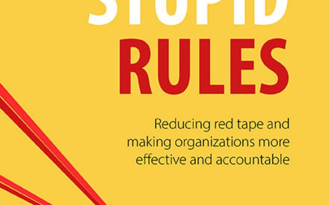 A businessman, attempting to leap forward, is held back by red tape.