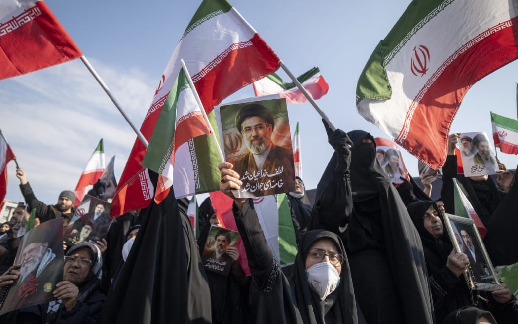 A veiled Iranian woman wears a protective face mask and holds up a portrait of Iran's new Supreme Leader, Ayatollah Mojtaba Khamenei, the son of the late Leader Ayatollah Ali Khamenei, during a rally to pledge allegiance to Mojtaba Khamenei amid the U.S.-Israeli military campaign in Tehran, Iran, on March 9, 2026. (Photo by Morteza Nikoubazl/NurPhoto) (Photo by Morteza Nikoubazl / NurPhoto via AFP)