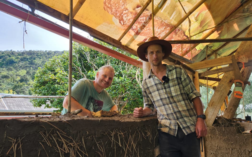 Two men leaning on a cob wall under construction