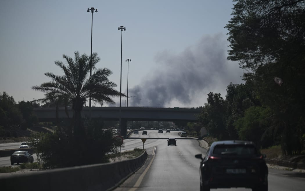 Motorists drive along a street as smoke rises from a reported Iranian strike in the area where the US Embassy is located in Kuwait City on March 2, 2026. Black smoke was seen rising from the US embassy in Kuwait City on March 2 after the latest volley of Iranian strikes, an AFP correspondent saw. (Photo by AFP)