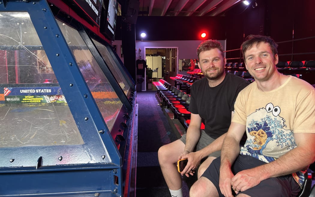 Picture shows two man sitting next to a bulletproof cage.