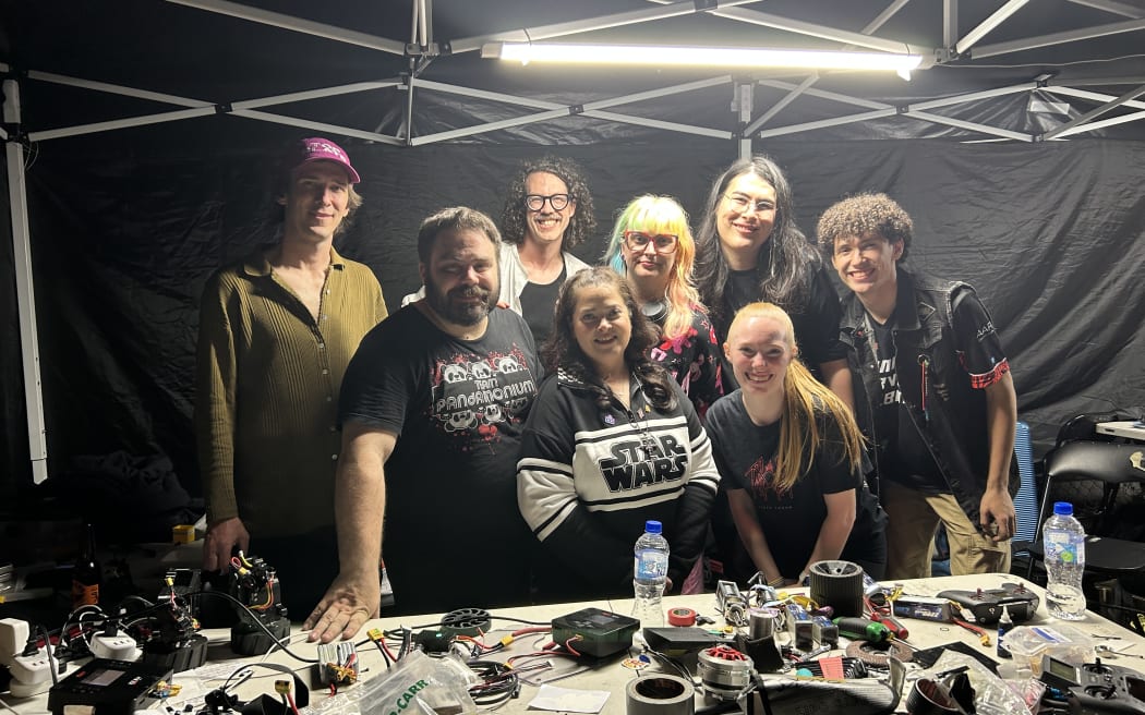 Picture of a group of eight people posing behind a desk full of gear.