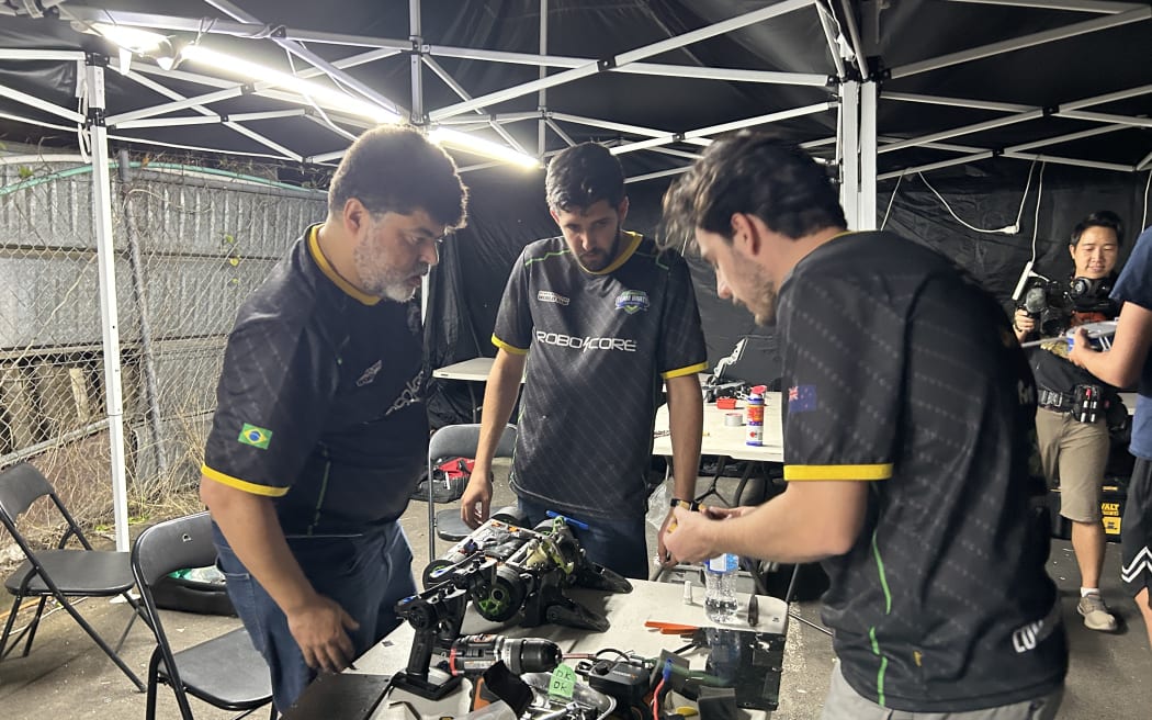 Picture of three people huddling around a desk full of parts and gears.