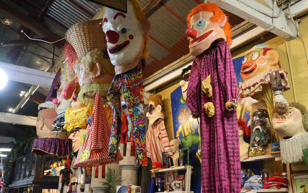 Picture of clown facemasks and costumes hanging from a shop ceiling.