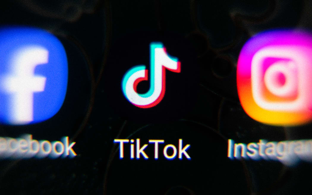 A close up of a phone screen with the icon for TikTok in the center, flanked by Facebook on the left and Instagram on the right.