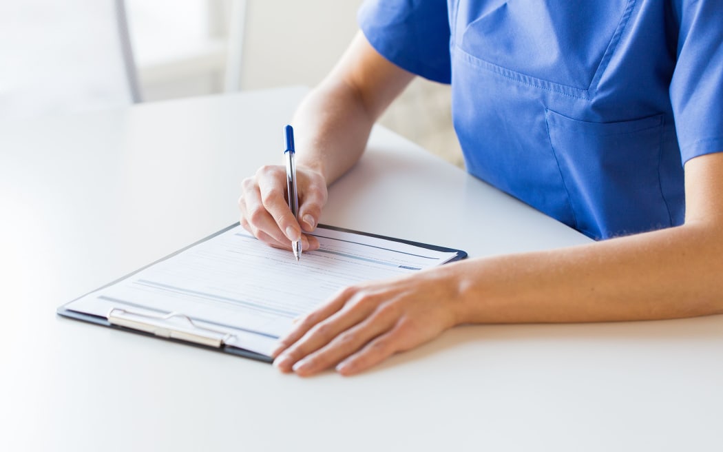 medicine, people and healthcare concept - close up of female doctor or nurse writing medical report to clipboard at hospital