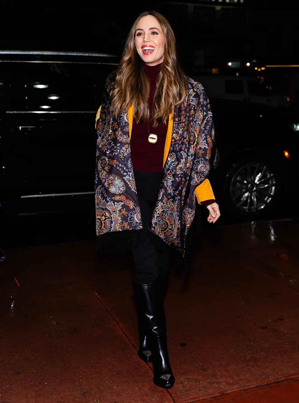 Eliza Dushku in a stylish shawl and knee-high boots walking, smiling for the camera