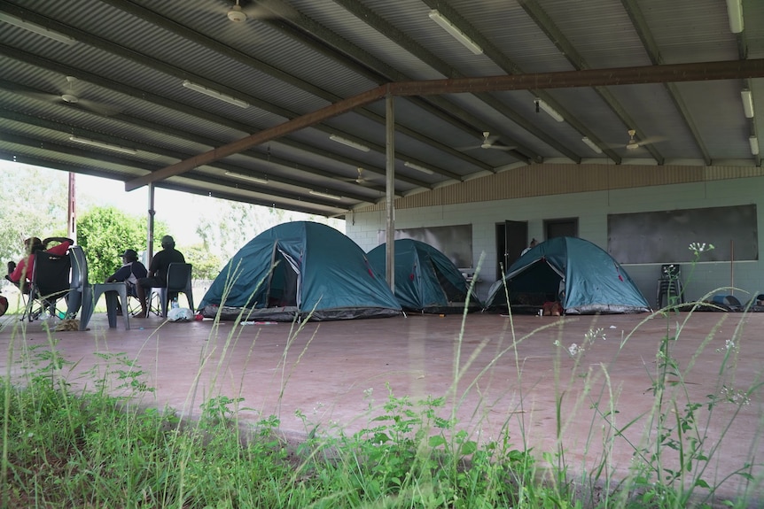 Tents set up under a shelter, and group of people sitting on campchairs