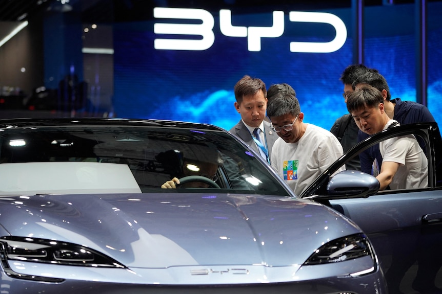 a group of men look at a BYD car in front of a BYD logo