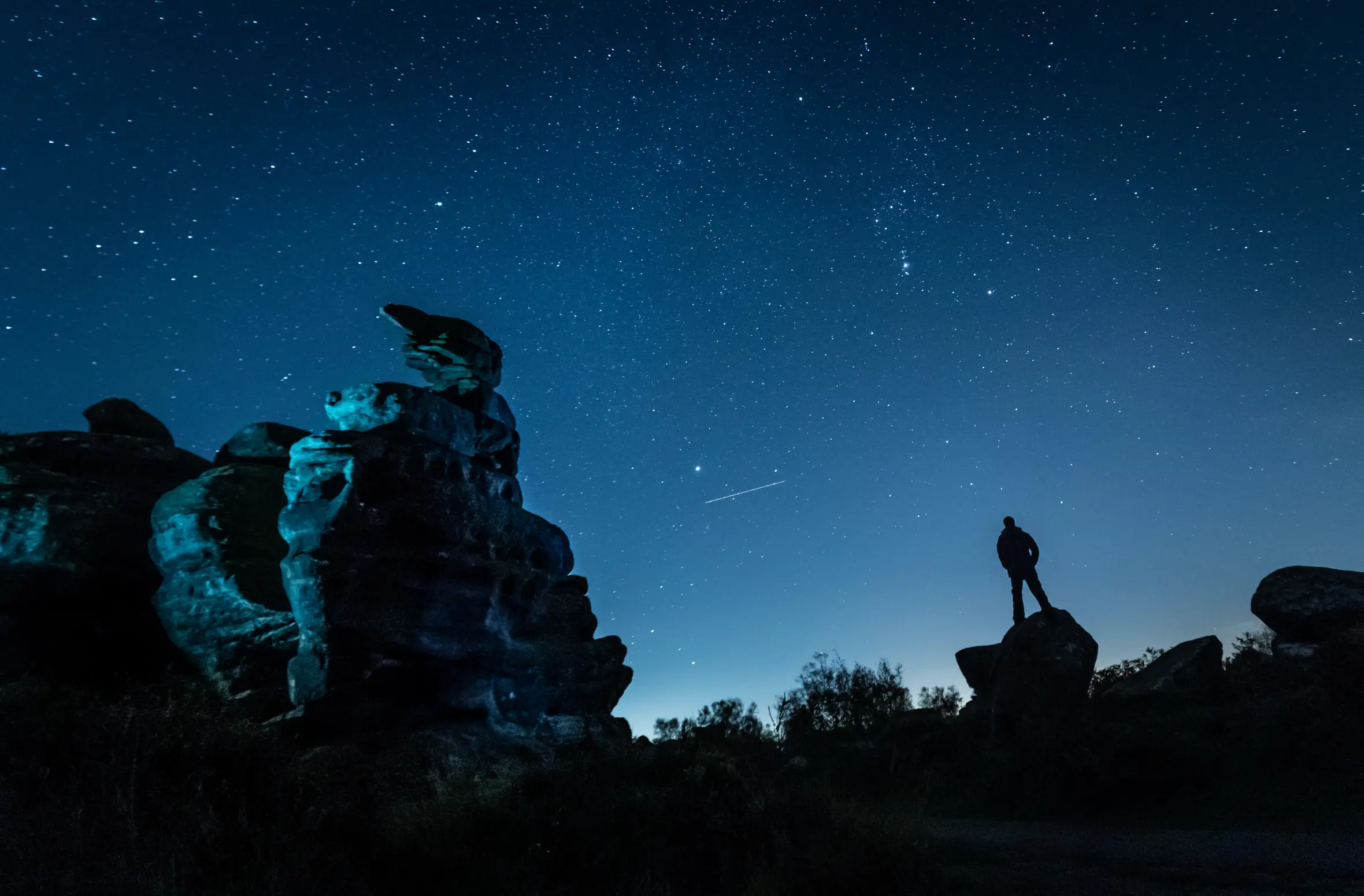 A person stargazing at Brimham Rocks in Yorkshire as a plane passes by during the Orionid meteor shower.