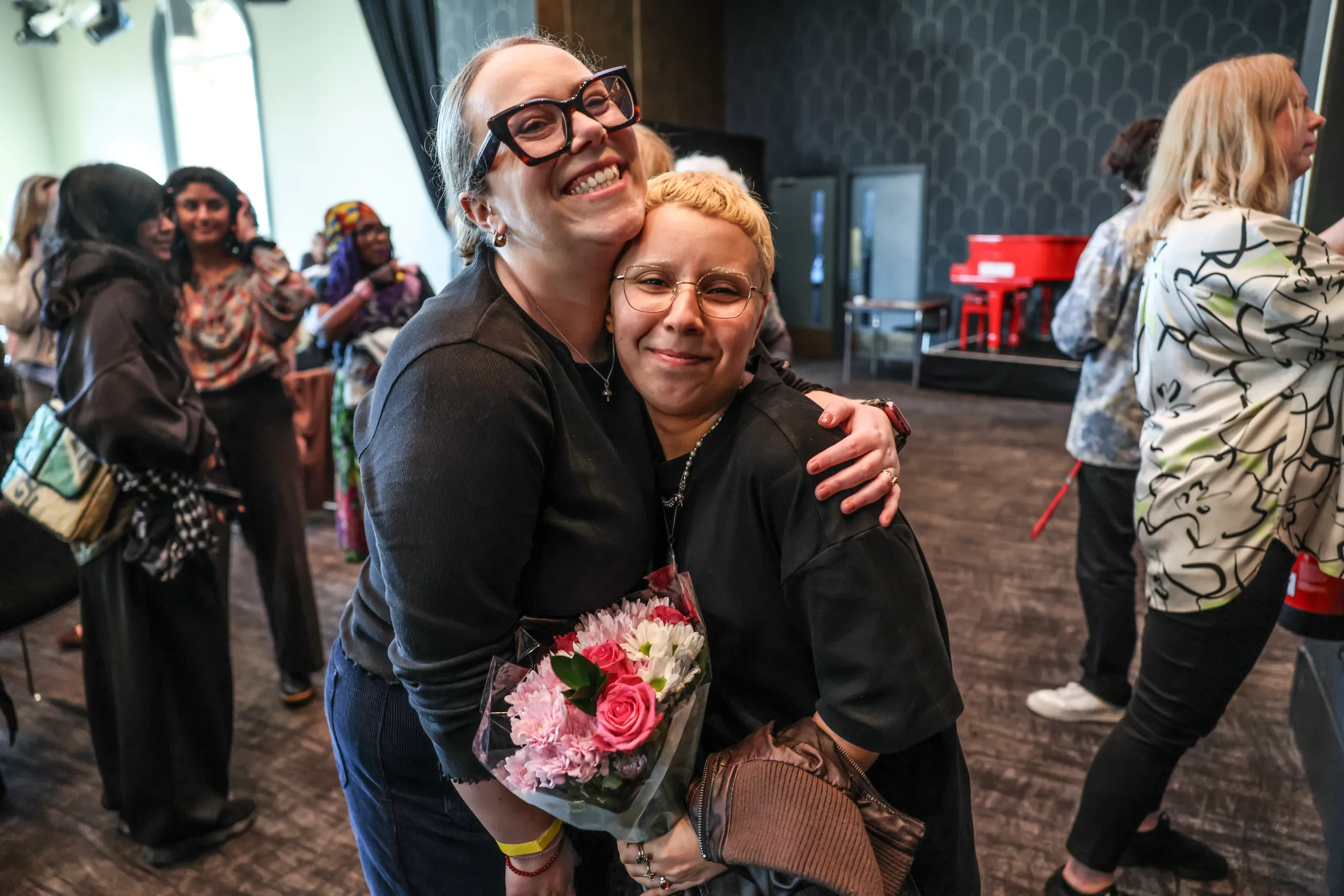 Carly Smallman hugs a woman with short blonde hair who is holding a bouquet of flowers, after a stand-up comedy performance.