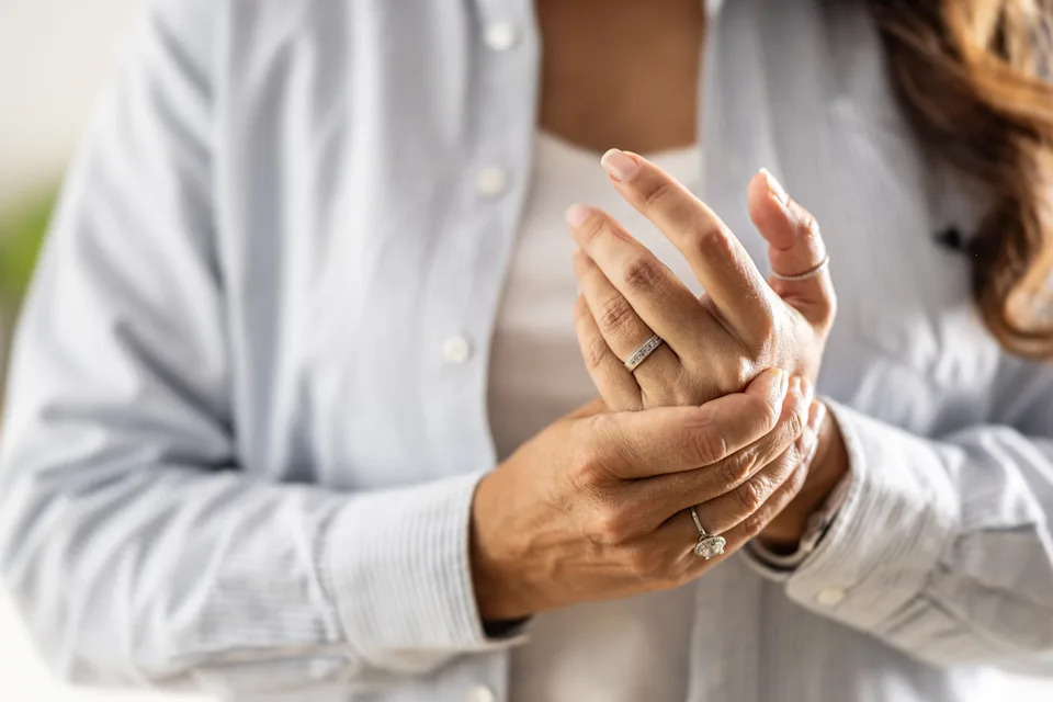 A person wearing a white shirt, touching their hands, adorned with rings