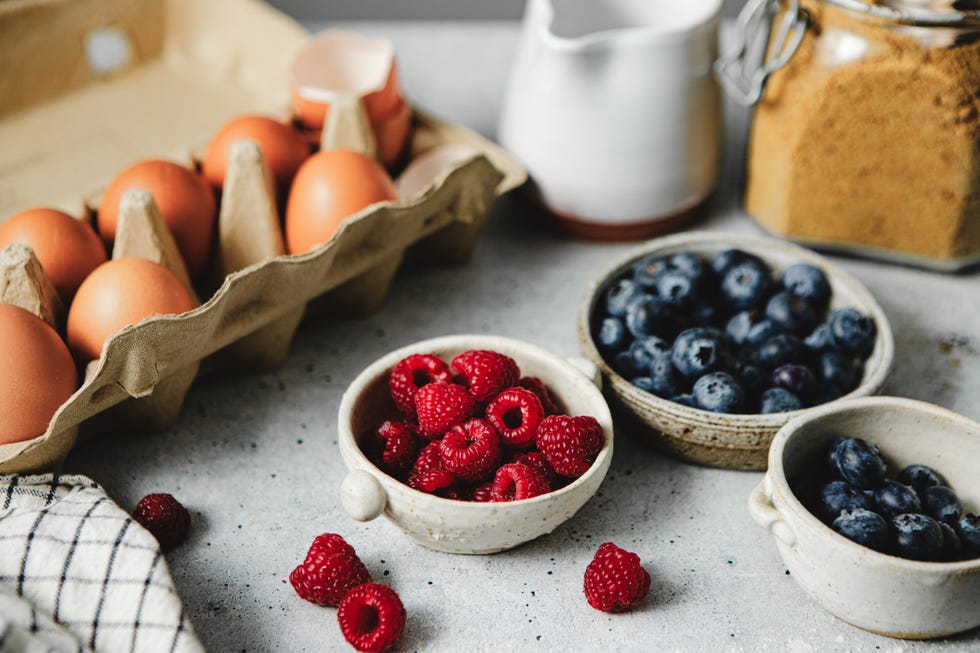 Close-up of food ingredients on kitchen counter for preparing healthy breakfast close up of food ingredients on kitchen counter for preparing healthy breakfast. brown eggs in a carton with raspberry and blueberries in bowls on kitchen table.