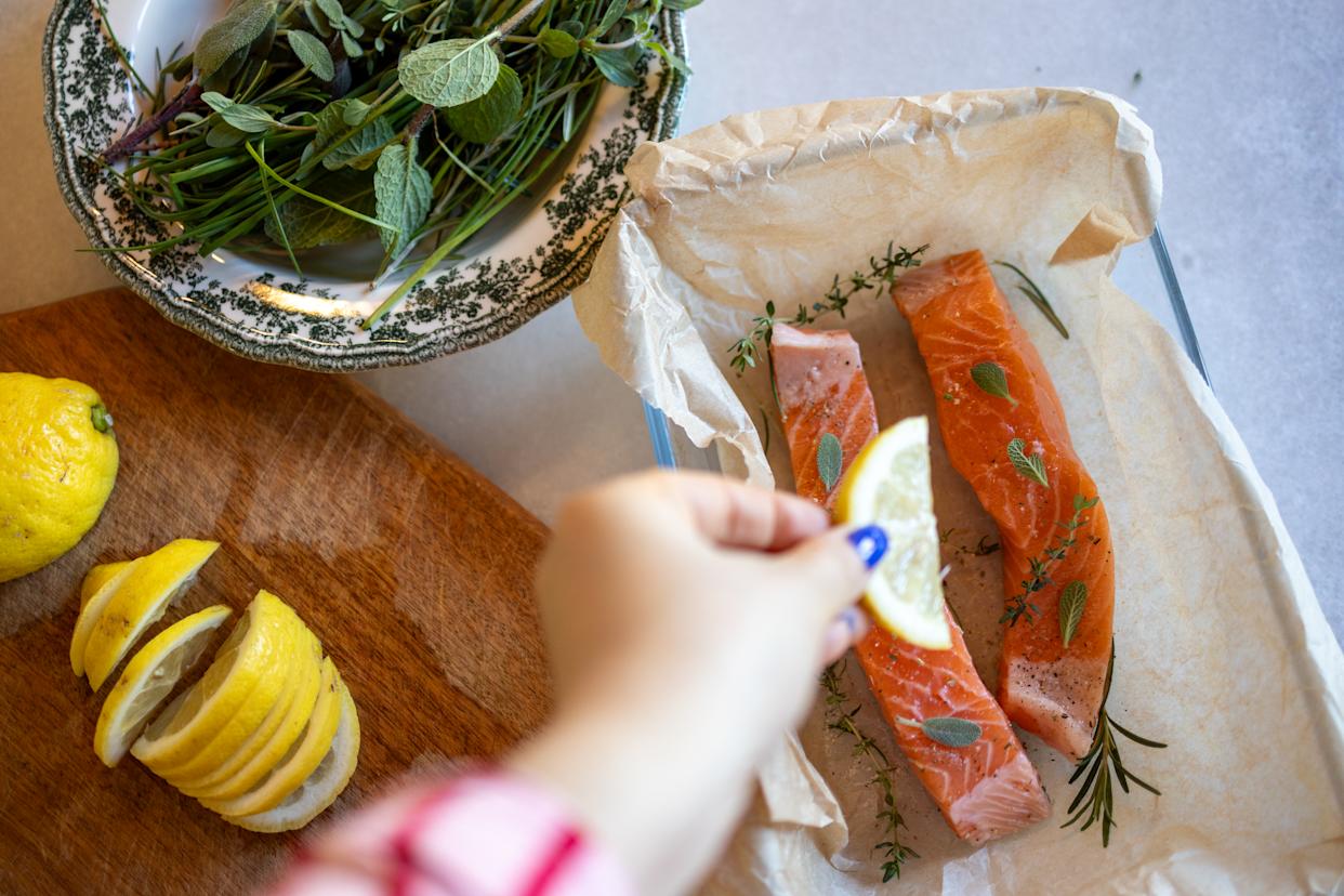 High angel view of raw salmon steaks decorated with different herbs and slices of lemon before baking. Some salmon cooking ingredients, such as lime, salt, pepper, different herbs, rosemary are  visible by side. Preparing food at home. Homemade