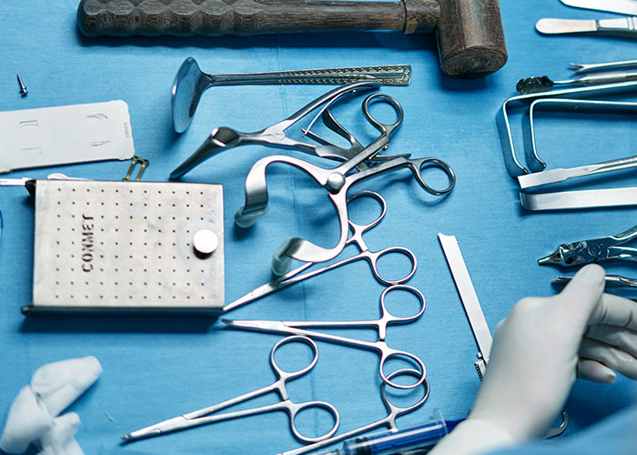 Surgical tools and medical instruments laid out on a blue drape with a gloved hand arranging them, medical secrets concept.