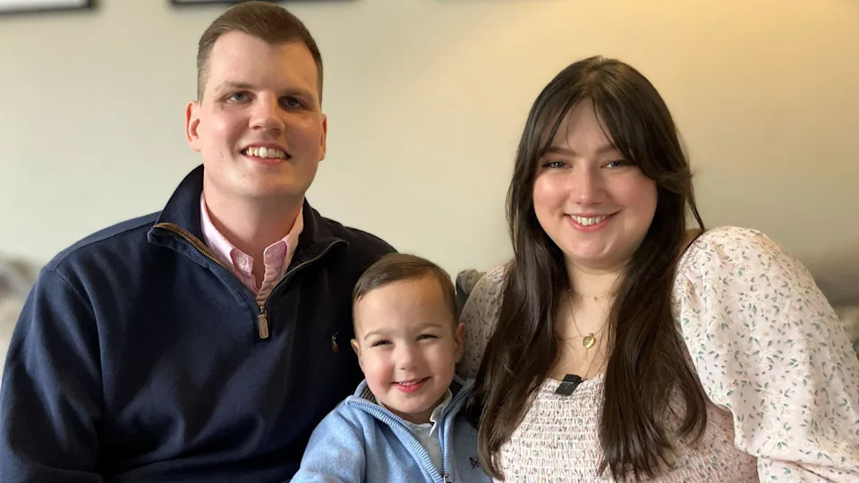 Alaric sits with his mother and father either side of him. All three are smiling broadly. 