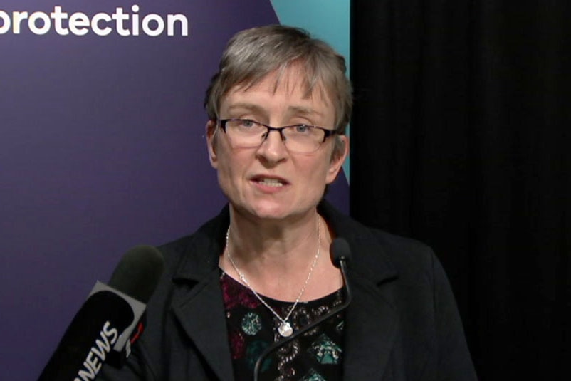 Dr Angie Bone speaking at a press conference, protection written behind, has short grey hair, glasses.