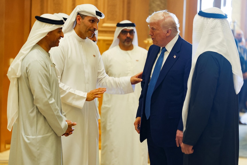 Donald Trump speaks with several men in kanduras, the traditional dress of Emirate men