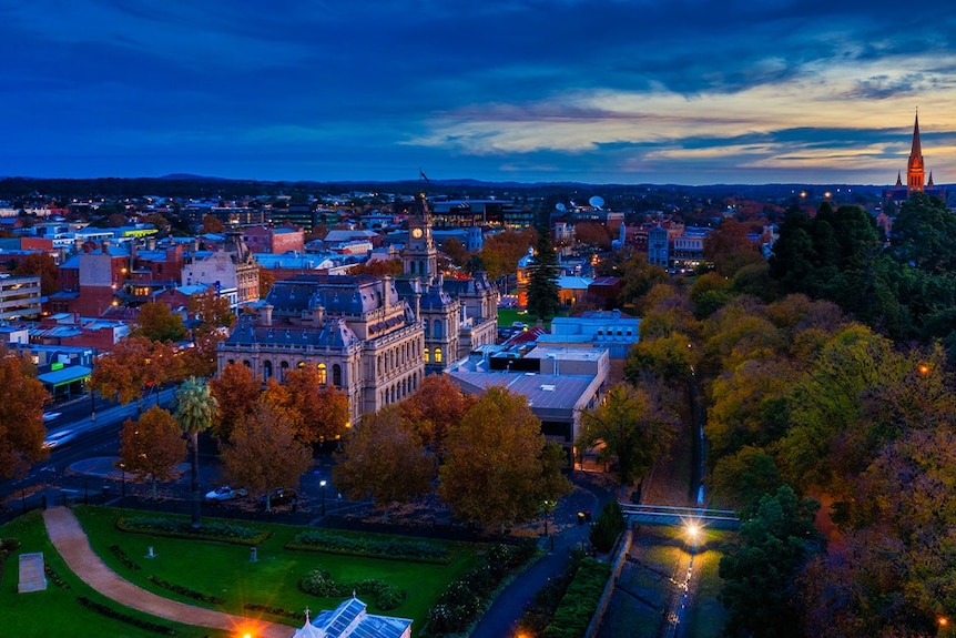 A large historic building among others in a city at dusk, as seen from a nigh vantage point.
